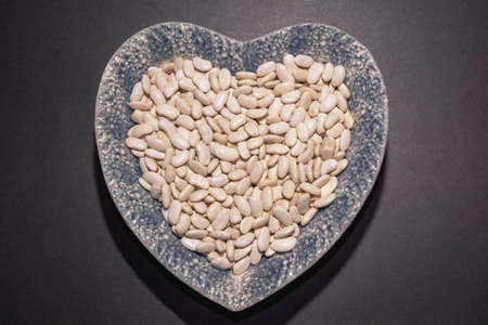White haricot beans in heart-shape plate on black table. Flat lay, copy spaceの写真素材