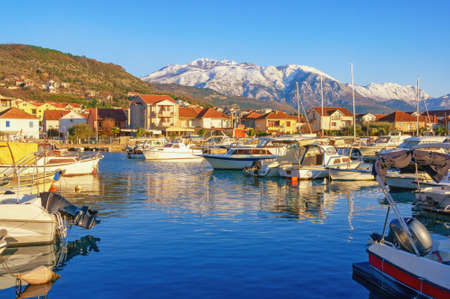 Beautiful Mediterranean landscape on sunny winter day. Fishing boats in harbor and snow-capped mountains. Montenegro, Kotor Bay. Tivat city,  view of marina Kalimanj and mountains of Lovcenの写真素材