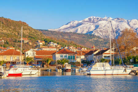 Sunny winter day, beautiful Mediterranean landscape. Green town and fishing boats in harbor against snow-capped mountains. Montenegro,  Bay of Kotor. Tivat city,  view of marina Kalimanj and mountains of Lovcenの写真素材