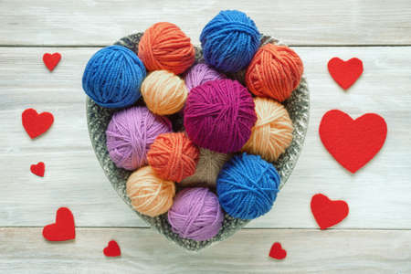 Colorful balls of wool in heart shaped plate on rustic table. Hobbies and knitting conceptsの写真素材