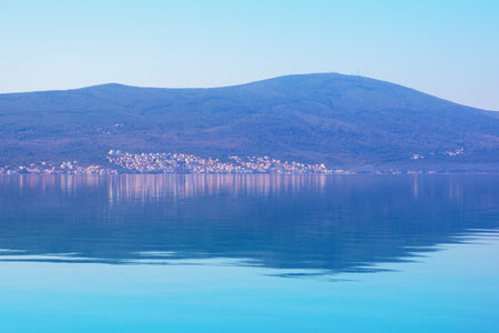Reflection. Mountain and  small village are reflected in blue water. Blue background. Space for text. Montenegro, Kotor Bayの写真素材