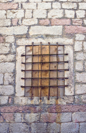 Boarded up window with metal grid in stone wall