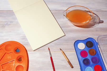 Watercolor painting. Sketchbook, watercolor paints, palette and cup of water on rustic table.  School concept. Free space for text or imageの写真素材