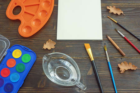 Watercolor painting. Open sketchbook, palette, cup of water, paintbrushes and pencil on rustic table.  School concept. Free space for text or pictureの写真素材