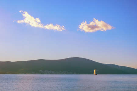Blue sky and white clouds, white sailboat on blue water. Minimalistic landscape. Travel and vacation concepts.  Montenegro, Kotor Bayの写真素材