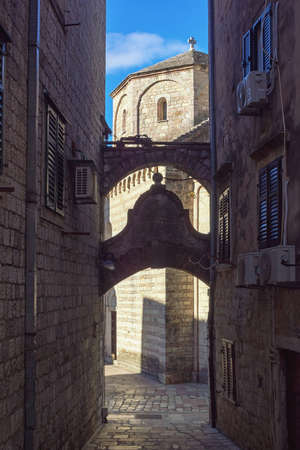 Montenegro. Narrow street of Old Town of Kotor on sunny winter day. Ancient buildings, church.  Church of St. Mary. Contrast of light and shadowsの写真素材