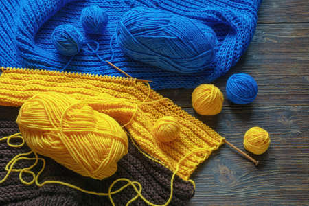 Hobbies concept. Unfinished knitting, blue and yellow skeins  of wool and knitting  needles on rustic tableの写真素材