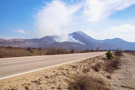 Balkan road trip. Landscape with road in valley of Dinaric Alps on sunny spring day. Clouds of smoke...