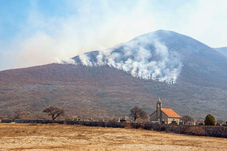 Clouds of smoke rise from mountain forest fire.  Valley of Dinaric Alps on sunny spring day. Bosnia and Herzegovina, Republika Srpska. Church of St.Petka, Grab, Zubciの写真素材