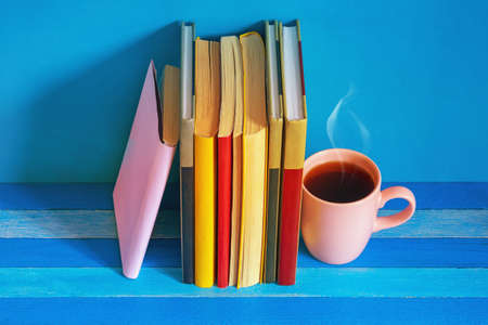 Different colorful books and cup of coffee on blue rustic table. Copy spaceの写真素材