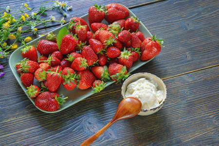 Plate with ripe strawberry and cup with sour cream on dark rustic table. Summer wildflowers. Free space for textの写真素材