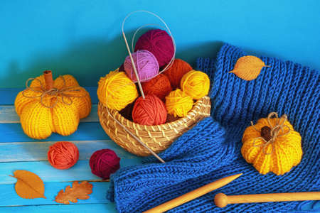 Autumn knitting and hobby concepts. Yellow knitted pumpkins, colorful balls of wool, warm scarf, knitting needles and autumn leaves on blue rustic tableの写真素材