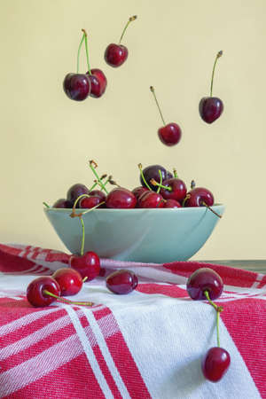 Fresh ripe cherries fall into a bowl on a rustic table. Ð¡opy spaceの写真素材