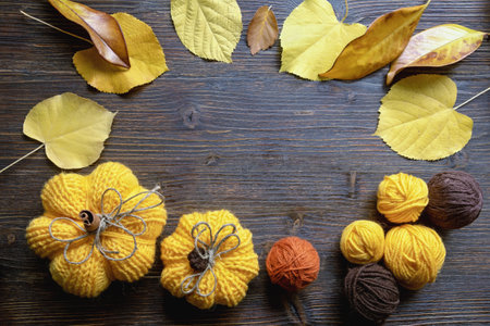 Autumn frame. Autumn leaves, balls of wool and knitted pumpkins on rustic table. Copy spaceの写真素材