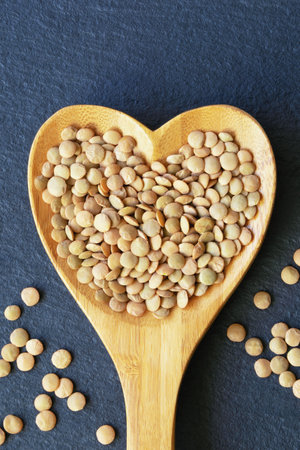 Lentils in heart shaped spoon on dark table. Flat lay, copy spaceの写真素材
