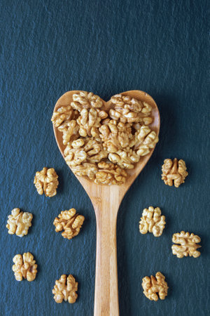Walnut kernels in a heart-shaped wooden spoon on a black table. Flat lay, copy space