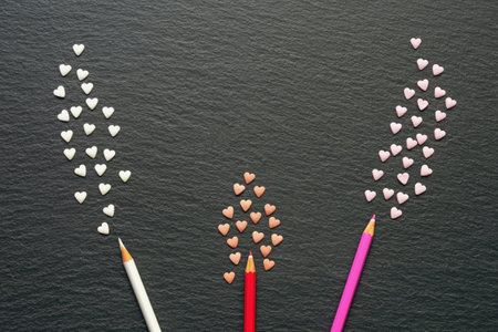 Color pencils and small colorful hearts on black background. Abstract bouquet, flat lay, copy spaceの写真素材