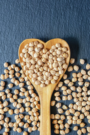 Chickpeas in a heart-shaped wooden spoon on a dark background. Flat lay, copy spaceの写真素材