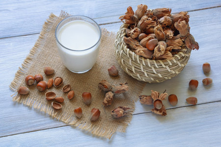 Nut milks. Glass of dairy-free alternative milk,  hazelnuts in small basket on rustic tableの写真素材