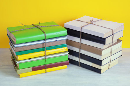 Two stacks of books tied with rope on rustic table. Yellow background, copy spaceの写真素材