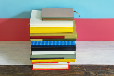 Stack of different books on rustic table. Pink and blue paper background, copy spaceの写真素材