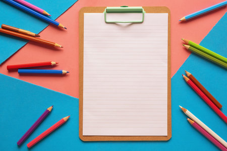 Clip board with a sheet of paper and colored pencils on a background of colored paperの写真素材