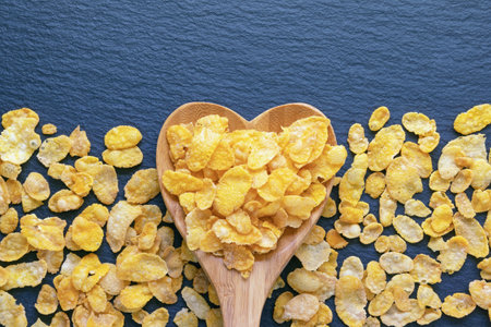 Corn flakes in heart-shaped wooden spoon and on dark table. Copy spaceの写真素材