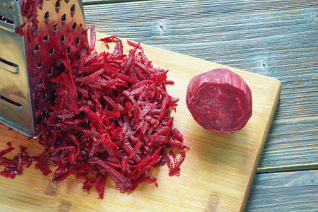 Grated red beetroot and grater on cutting board. Dark rustic table, copy spaceの写真素材