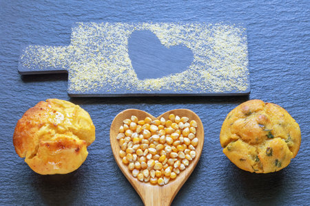 Corn kernels in heart-shaped wooden spoon. Corn flour muffins. Cornmeal on cutting board. Copy spaceの写真素材