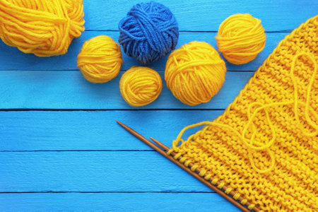 Hobbies and knitting concept. Yellow and blue balls of wool and  knitting needles on blue rustic table. Copy spaceの写真素材