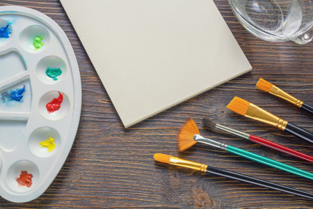 Sketchbook, palette, watercolor paints and different paintbrushes on  dark rustic table. Copy spaceの写真素材