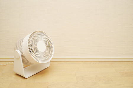 White electric fan on the floor in front of a white wall.の写真素材