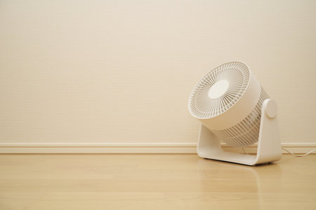 Modern electric fan on the floor in front of a white wall.