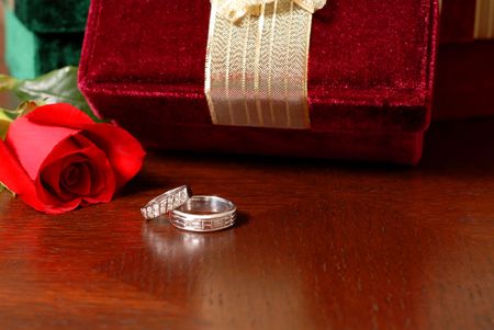 Wedding rings with Christmas gifts and a rose resting on a table