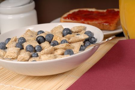 A bowl of wheat cereal with blueberries, toast and orange juice