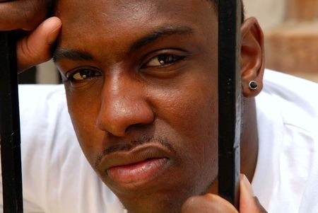 Young African American man with an angry expression looking between iron barsの写真素材