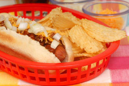 Chili cheese hot dog with onions served with potato chipsの写真素材