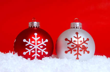 Two festive Christmas ornaments in snow with a red backgroundの写真素材