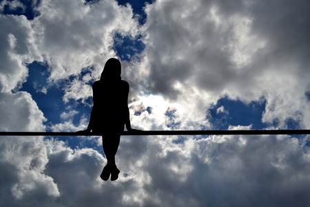 Girl silhouette sitting against cloudy sky background; peace conceptの写真素材