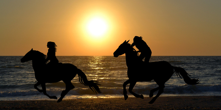Two horse riders silhouettes galloping on the beachの写真素材