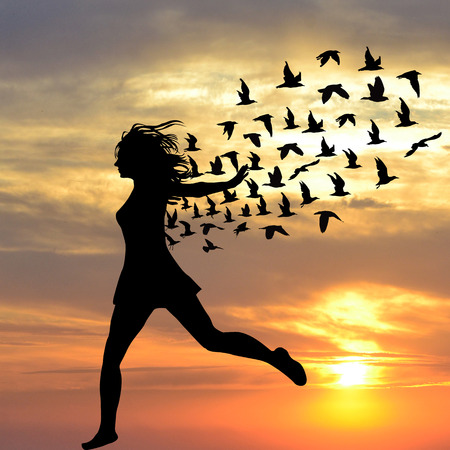Silhouette of young woman jumping with birds flying from herの写真素材