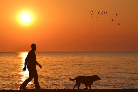 Silhouette of a man with his dog on the beach on sunriseの写真素材