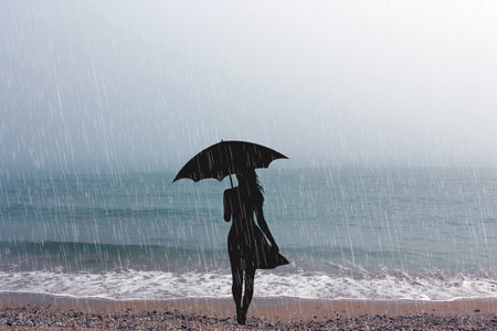 Romantic composition with a woman alone standing by the sea in the rain with an umbrellaの写真素材