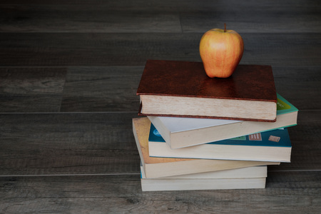 A pile of books with an apple on top on the wooden backgroundの写真素材