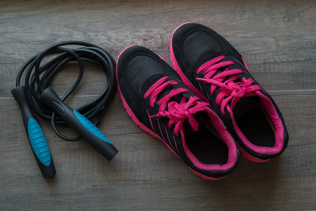 Pink sport shoes with jump rope on wooden background