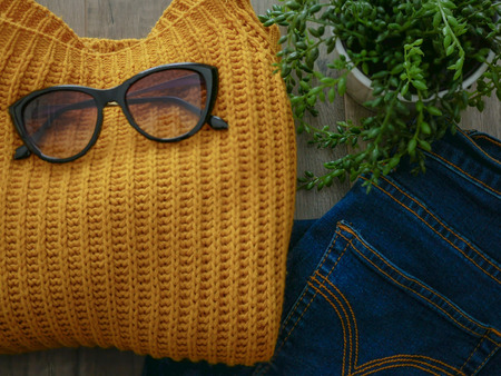 Flat lay of yellow winter cloth and jean on wooden tableの写真素材