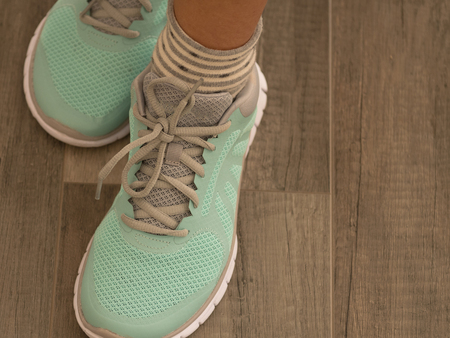 Woman wearing light green sport shoes on wooden floorの写真素材