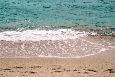 Footsteps in the sand on the beach, about to be wiped out by a wave