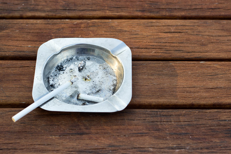 Metal ashtray with cigarette on wooden tableの写真素材