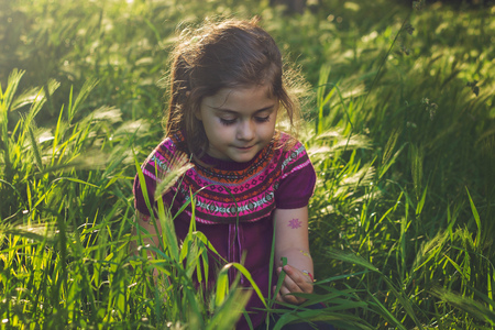 Beautiful little girl sitting in the grass on sunsetの写真素材